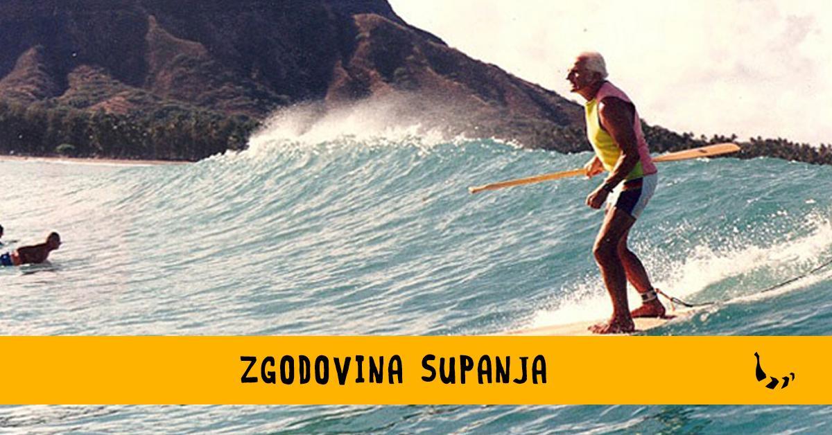 Starejši moški z veslom v roki stoji na deski, s katero surfa po valovih